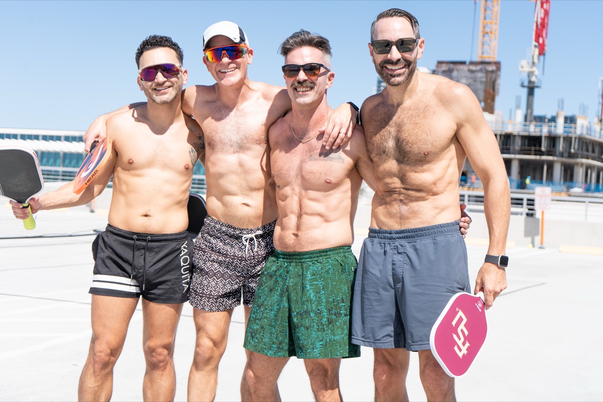 Four friends from our queer pickleball meetup with paddles, arms around each other in the sun